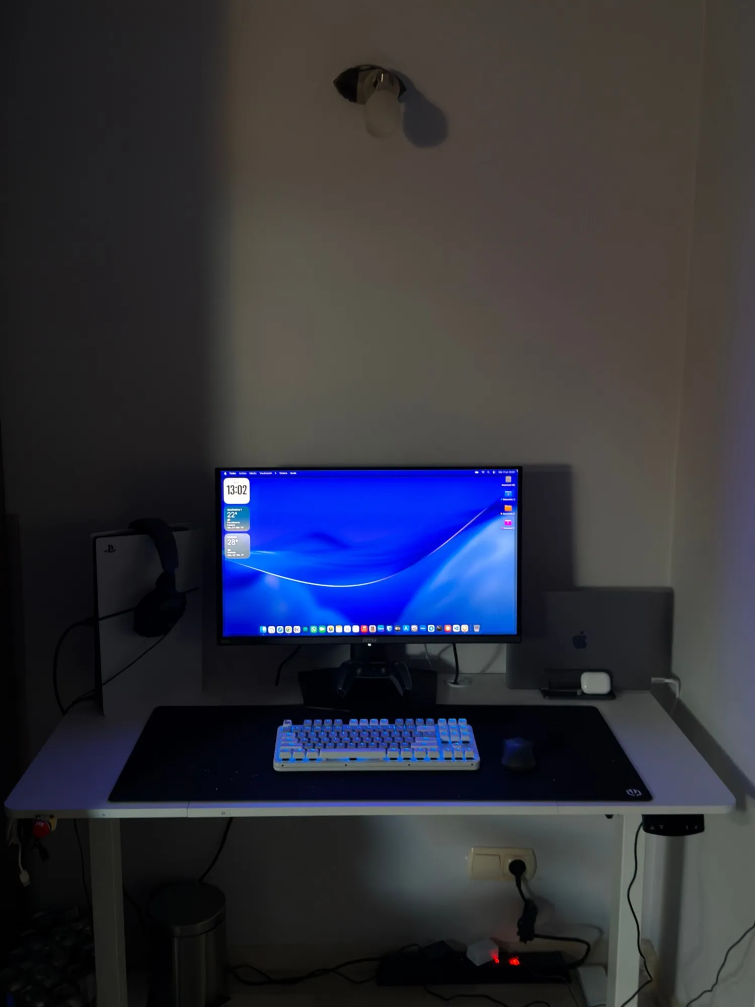 Mi escritorio con el monitor encendido y la habitación en penumbra